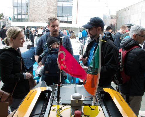 MIT AUV Lab's Paul Robinette talks to a couple with a baby about a yellow AUV on display