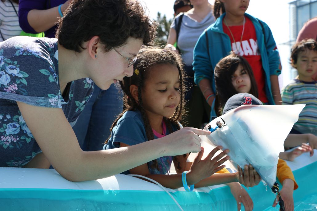 An MIT Sea Grant student holds a robotic manta with a young girl, pointing to its motors