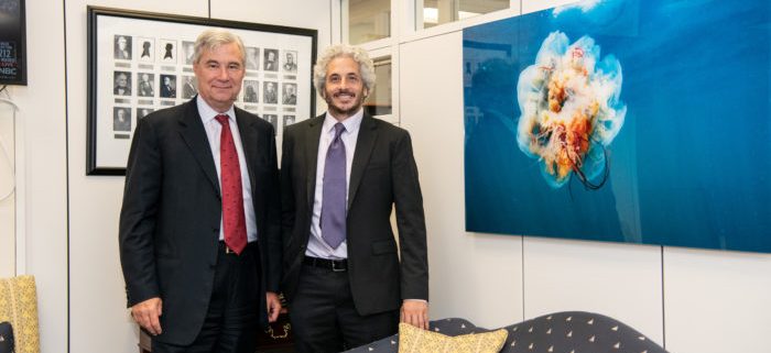 Senator Whitehouse meets and Keith Ellenbogen stand next to a large image of a jellyfish floating in blue water.