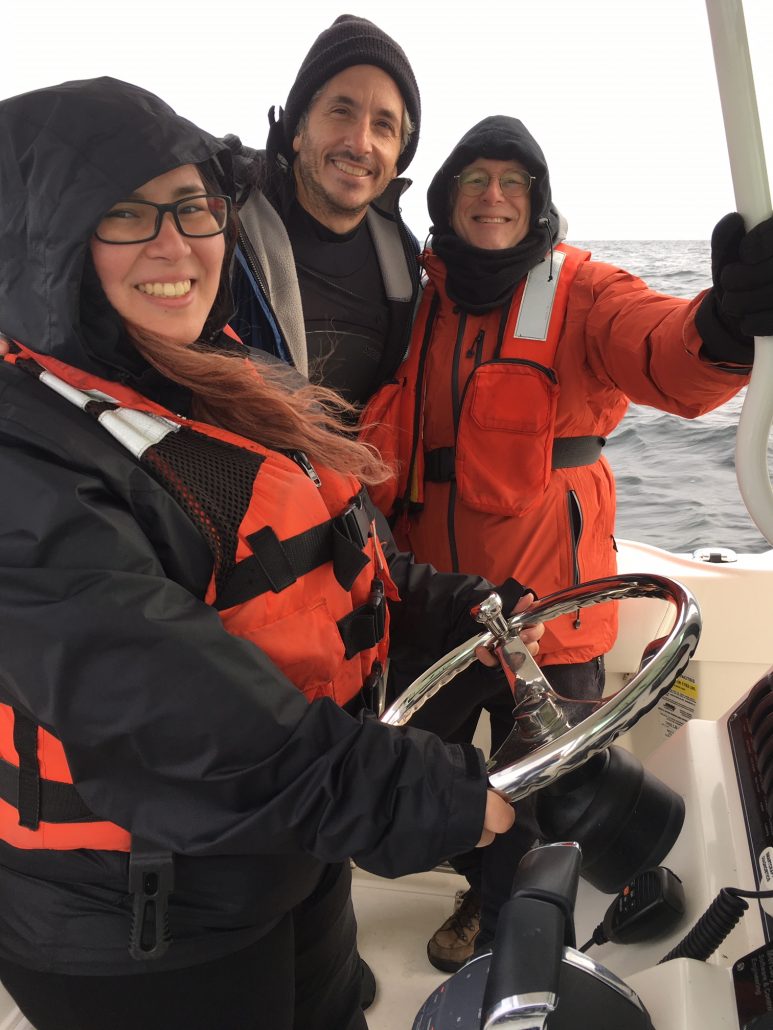 An MIT undergraduate student drives a boat with two MIT Sea Grant staff members