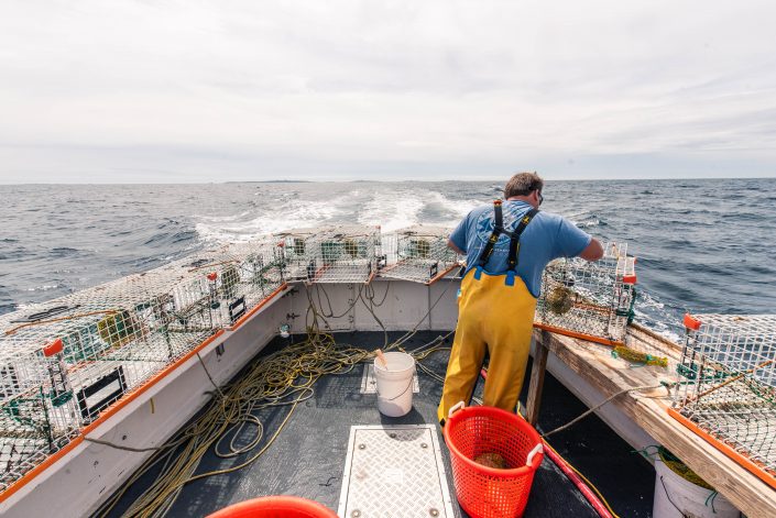 A deckhand on a lobster fishing vessel preparing equipment at sea.