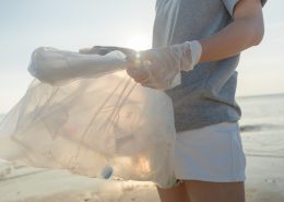 A person holds a plastic bag on the shore of a beach.
