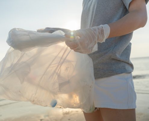 A person holds a plastic bag on the shore of a beach.